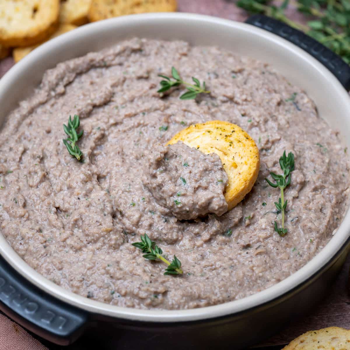 Creamy vegan mushroom pâté in a white bowl, garnished with thyme and served with crostini.